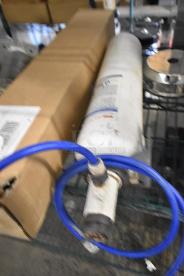 Six various water filter cartridges with connected blue hoses, condition unclear. Includes a labeled box and metallic component.