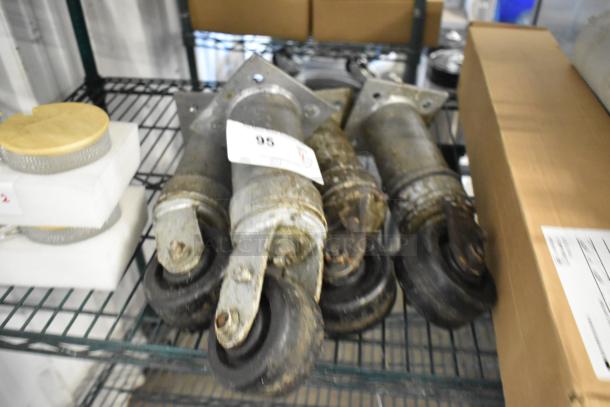 Lot of 4 commercial casters, used condition, with metal brackets and rubber wheels; visible wear and rust present.