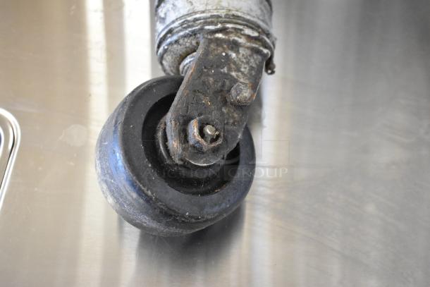 Lot of 4 commercial casters, used condition, metal frame with black rubber wheel, some rust visible.