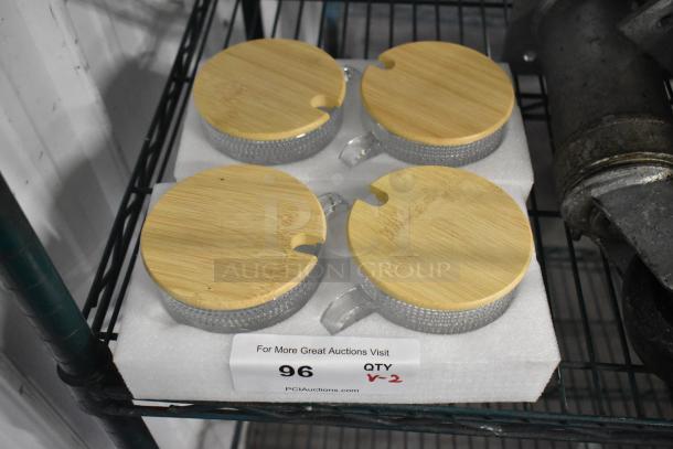 Lot of 4 brand new glass mugs with wooden lids, in pristine condition. Mugs feature textured glass and secure wooden tops.