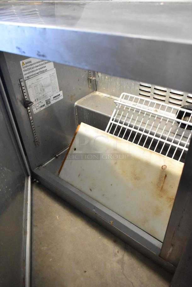 2023 Sir Lawrence SLMPREP-2DW stainless steel prep table interior, showing cutting board and wire rack. Some wear visible.