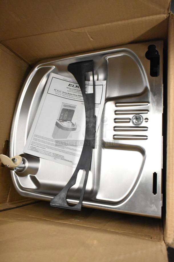 Alt Text: Elkay 438ESDWK stainless steel wall mount water fountain, 115V, 1 phase, new with minor scratches, in original packaging.