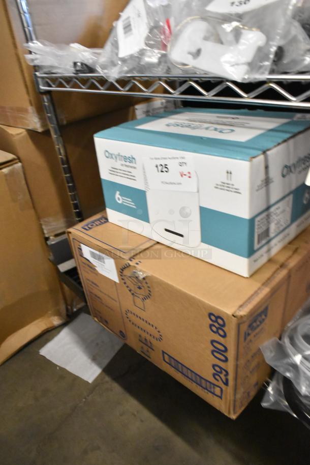 Boxes of Tork Universal paper towels and Oxyfresh air freshening system on a shelf, new condition, auction label visible.