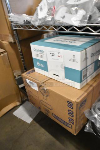 Boxes of Tork Universal paper towels and Oxyfresh air freshening system on a shelf, new condition, auction label visible.