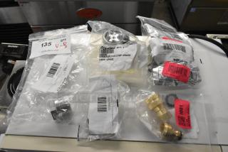 Set of 5 brand new scratch and dent items including a Regency spray nozzle adapter, Avantco screw cover, Cleveland fitting, and Fryclone valve. Labels visible.