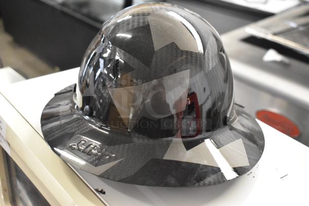 "Brand new black carbon fiber helmet with geometric design, featuring a cap-style brim. Mint condition, part of a scratch and dent auction lot."