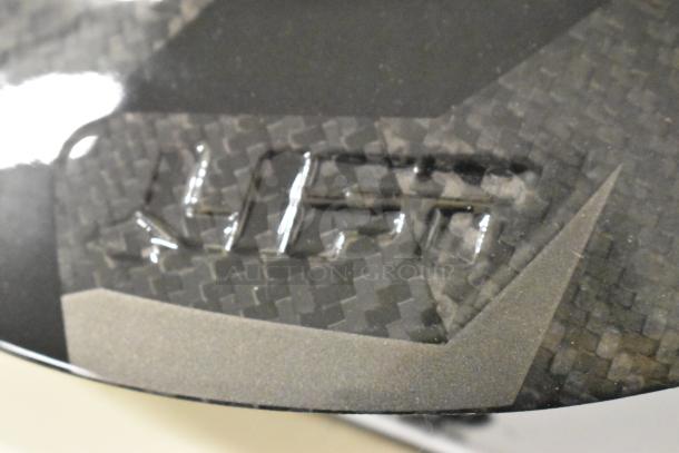 Carbon fiber helmet with geometric pattern, slight scratch marks, and embossed detail. New, minor cosmetic flaws.