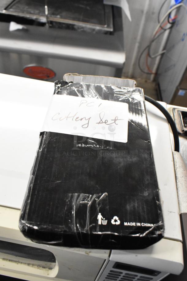 Black box labeled "Cutlery Set" with protective wrap. Visible "Made in China" marking. Slight box damage indicates scratch and dent.