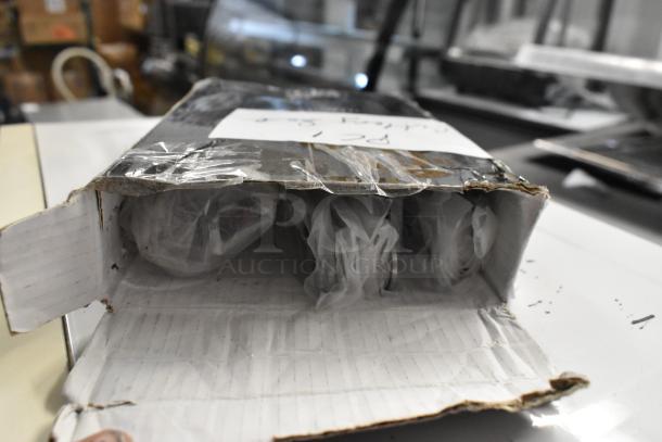 Open box containing three scratch and dent items: helmet, Cambro CFPFRC10135 cold fest pump, and cutlery set, wrapped in plastic.