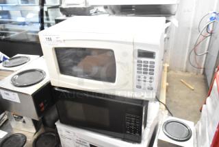 Two countertop microwave ovens with plates, models RGTM701 and MS8436127995-01, 120V, 1 phase. Visible wear.