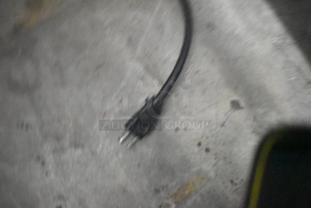 Blurred image of an electrical plug on a concrete floor, possibly related to an appliance or machine.