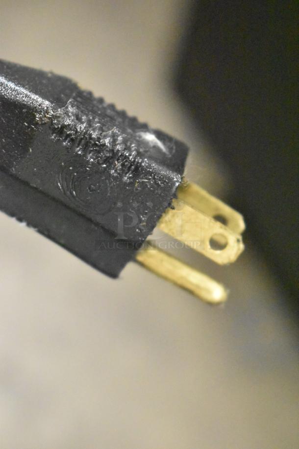 Close-up of a black power plug from a metal commercial waste oil caddy, featuring three prongs; 115 volts, 1 phase.