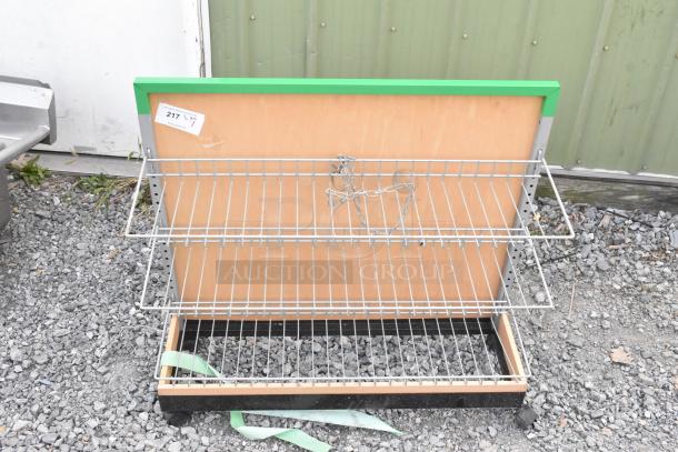 Shelving unit on casters with two wire racks, wood panel backing, and metal frame. Attached green trim. Includes item tag labeled "217."