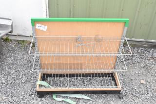 Shelving unit on casters with two wire racks, wood panel backing, and metal frame. Attached green trim. Includes item tag labeled "217."
