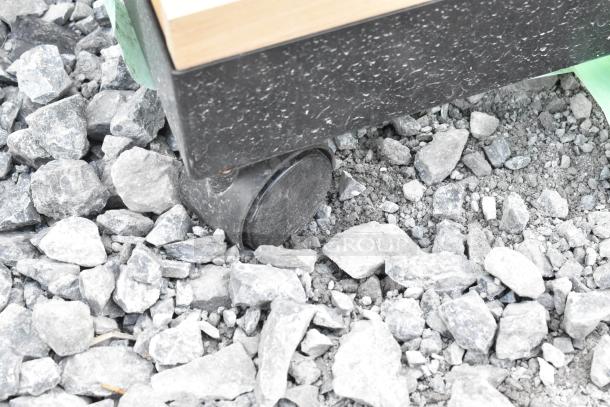 Shelving unit caster on gravel, showing black wheel and base, indicating mobility and rugged construction.