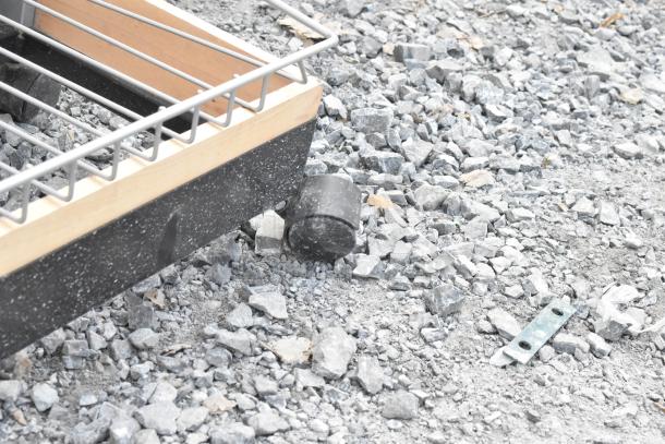 Shelving unit on casters, featuring a metal frame and wood accents, set on a gravel surface.