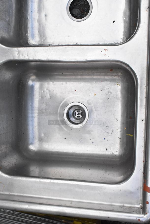 Stainless steel 3 bay sink, no legs, with visible drain openings, minor surface wear.