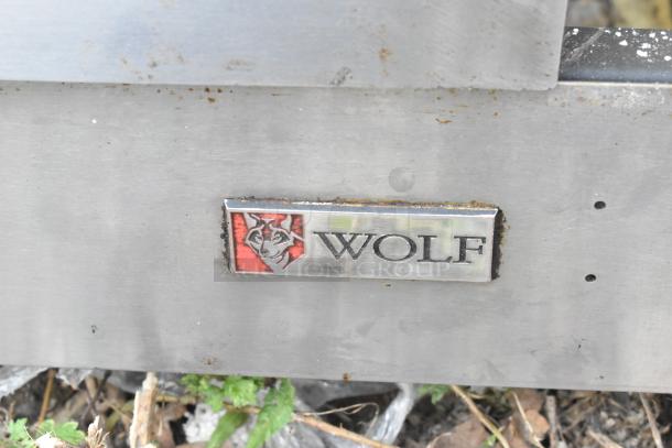 Wolf stainless steel commercial flat-top griddle, natural gas-powered, with visible logo. Some rust and wear present.