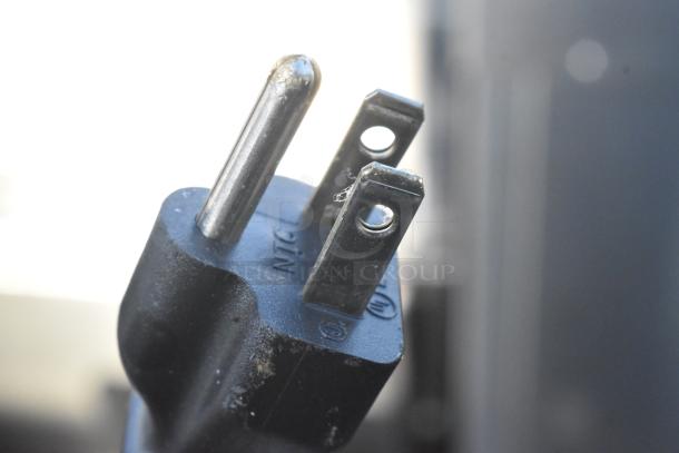 Close-up of a three-prong electrical plug against a plain background, likely indicating power specifics for an appliance.