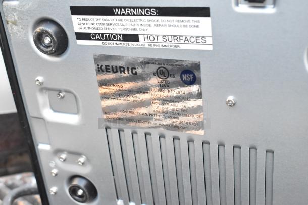 Labels on Keurig K150 coffee machine back panel, listing model, 120V, non-serviceable, NSF certified, and caution warnings.