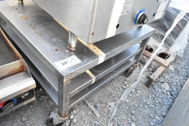 Stainless steel equipment stand with two under shelves on commercial casters, visible wear and rust, tag reads "237 QTY 1".