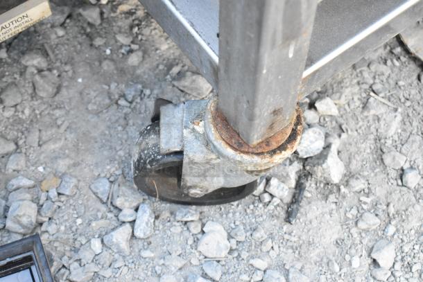 Stainless steel equipment stand with two under shelves on commercial casters, showing signs of wear and rust.