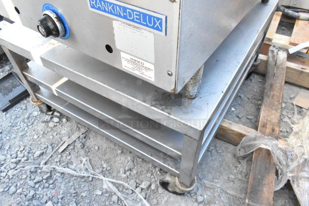Stainless steel equipment stand with two under shelves, commercial casters, "Rankin-Delux" branding visible.