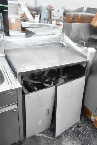 Stainless steel counter with under shelf, two doors, and commercial casters, showing visible wear and water droplets.