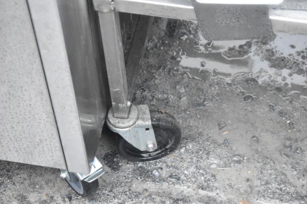 Stainless steel counter with under shelf, two doors, on durable commercial casters, suitable for heavy-duty use.