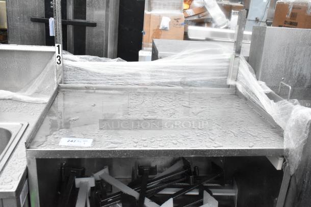 Stainless steel counter with under shelf, two doors, and commercial casters. Surface shows water droplets, indicating outdoor storage.