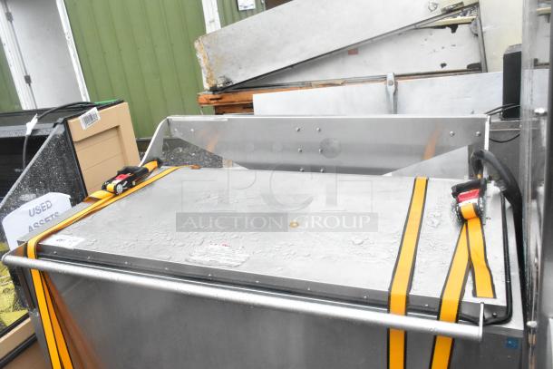 Stainless steel commercial washing/soaking tub, secure with yellow straps, in used condition, outdoor setting.