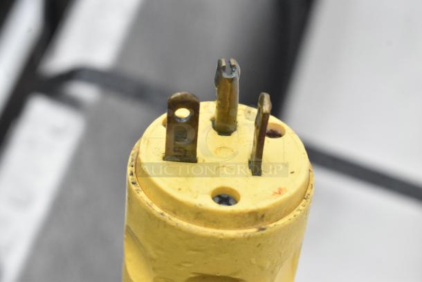 Yellow industrial power plug with three metal prongs, slight wear visible, suitable for commercial equipment.