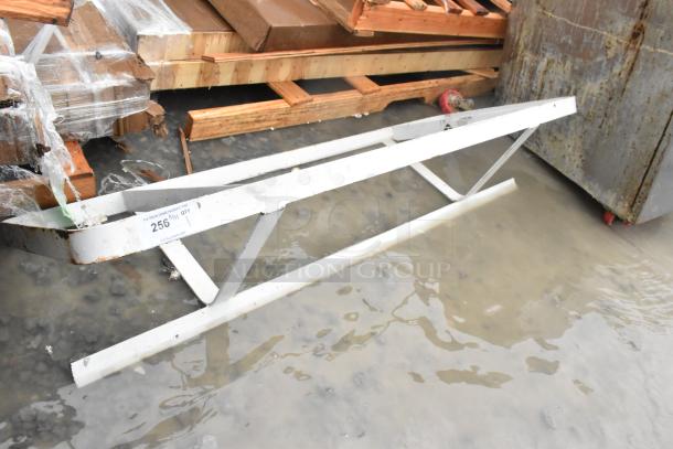 Metal pot rack, sturdy construction, placed on wet ground. Features white paint, minor rust, and attached auction label.