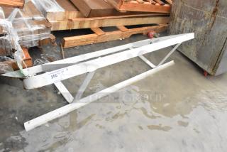 Metal pot rack, sturdy construction, placed on wet ground. Features white paint, minor rust, and attached auction label.