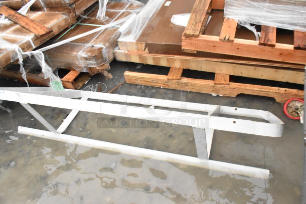 White metal pot rack, slightly rusted, lying outdoors near wooden pallets. Condition: used, with visible wear.