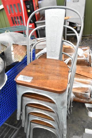 Stack of five gray metal dining chairs with wooden seats, in good condition. Each seat has a visible label with auction details.