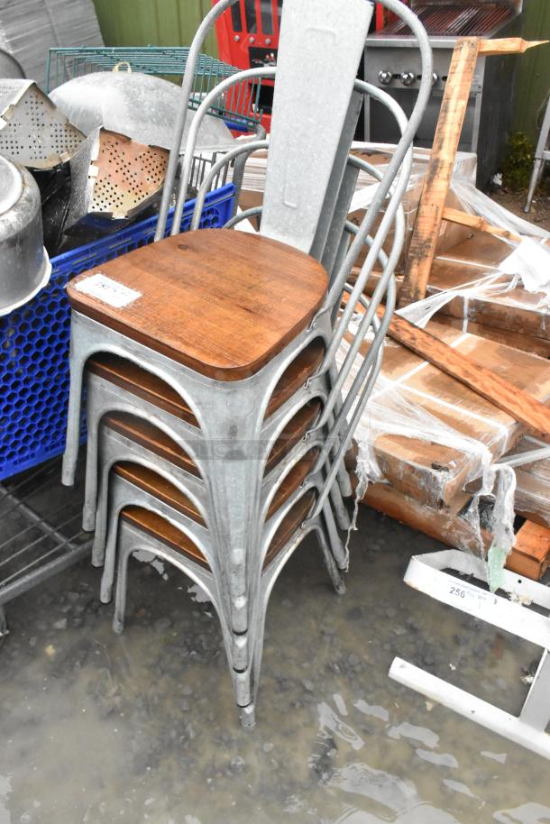 Stack of five gray metal dining chairs with wooden seats, auction lot with visible water exposure and warehouse setting.