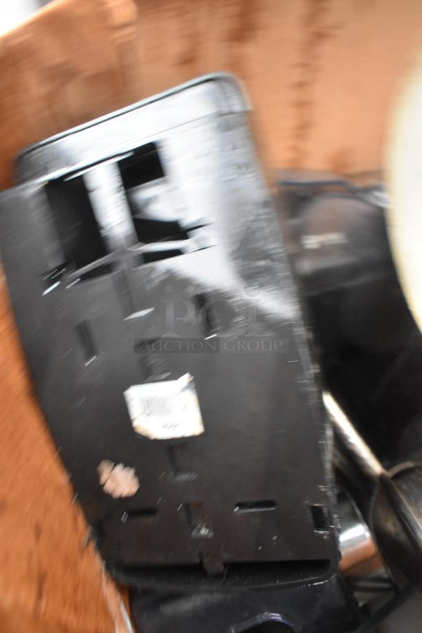 Blurred image of a black napkin dispenser with visible scratches and adhesive residue, part of a mixed auction lot.
