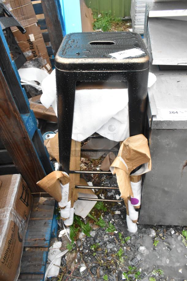 Three black metal Tolix style bar stools, brand new with some scratches and dents, partially wrapped for protection.