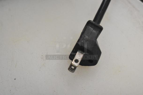 Power cord plug of Robot Coupe R2NCLR food processor, 120V, 1 phase. Shows wear, intact prongs, black casing.