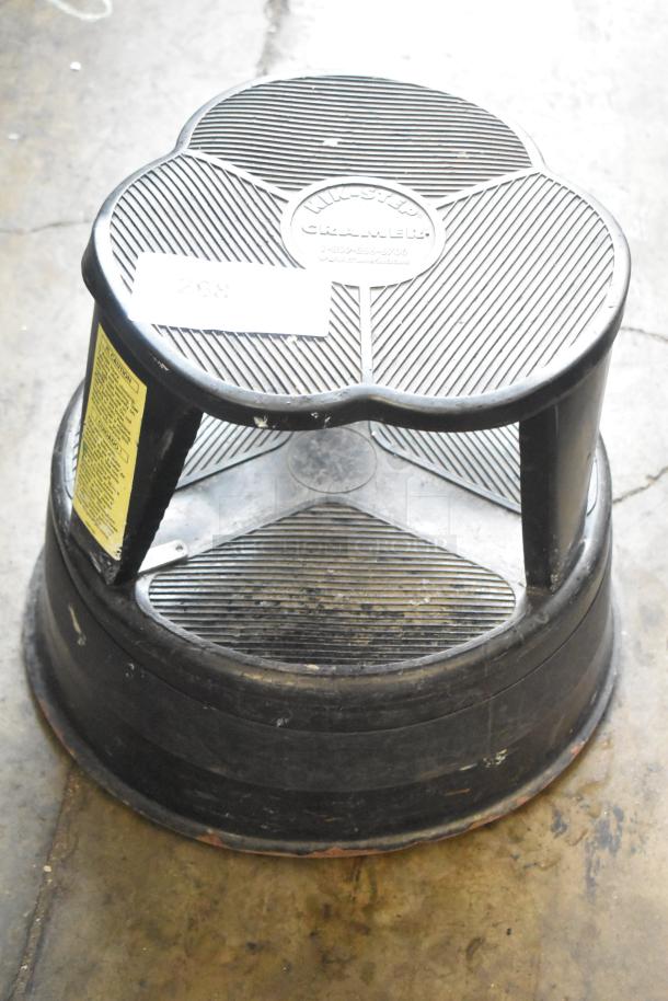 Black Poly Stool with ribbed surface and visible brand marking. Used condition. Yellow label with safety information attached.
