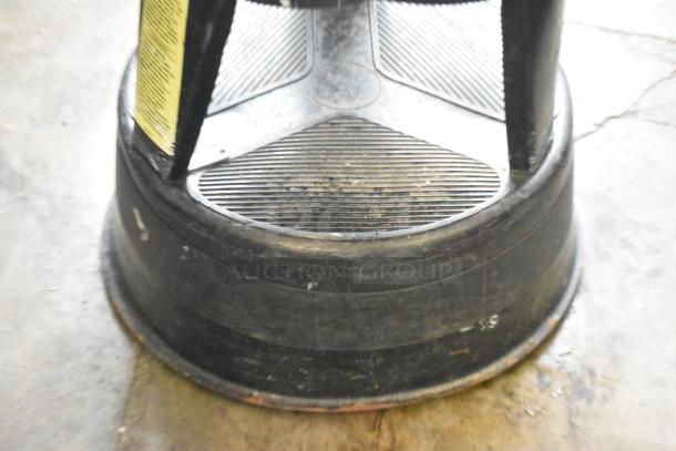 Black poly stool with ribbed texture, minor surface wear, and visible yellow safety label. Durable design ideal for seating.