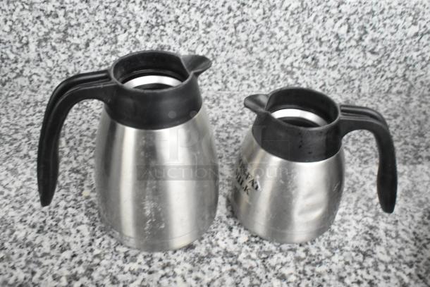 15 metal pitchers with black handles, varied designs, light wear, some with labeling, ideal for multipurpose use.
