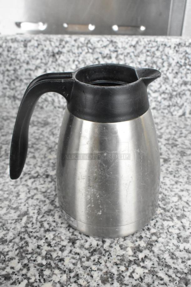 Stainless steel pitcher with black plastic handle, visible scratches, used condition. Part of a 15-piece metal pitcher set.