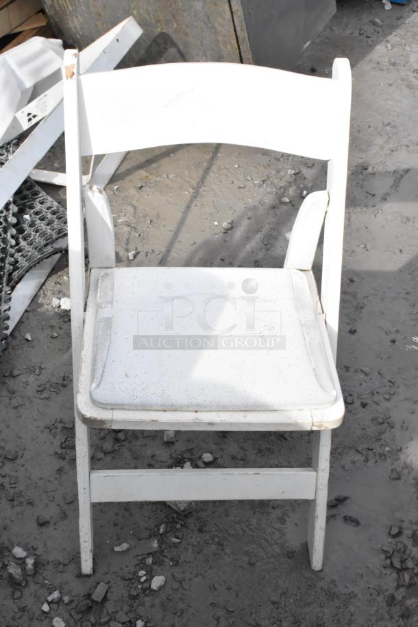 White folding chair shown outdoors, features visible signs of wear with scratches and dirt. Multiples available for auction.
