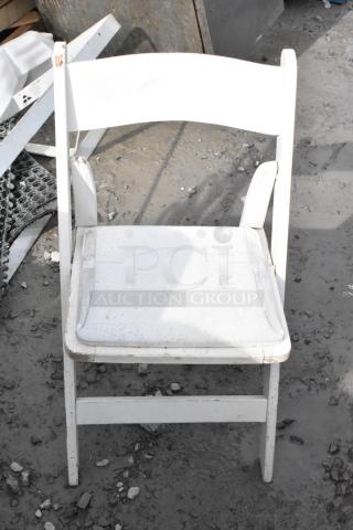 White folding chair shown outdoors, features visible signs of wear with scratches and dirt. Multiples available for auction.