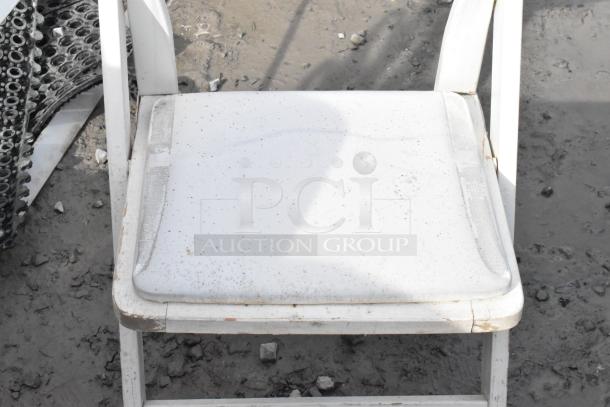 White folding chair with noticeable wear and dirt marks, set on outdoor ground. Part of a lot of six items.