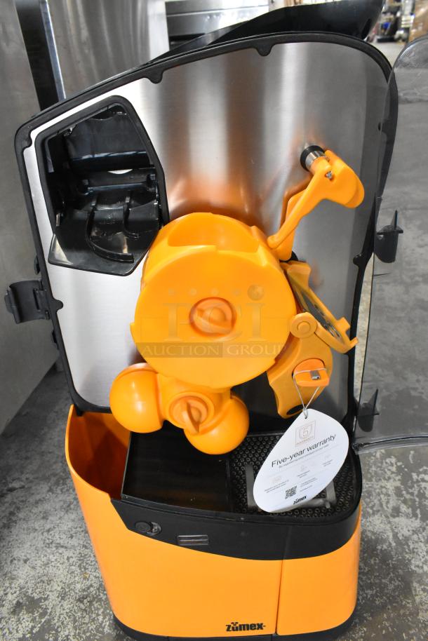 2025 Zumex MINEX metal citrus juicer, countertop model. Orange and stainless steel finish, includes five-year warranty tag.