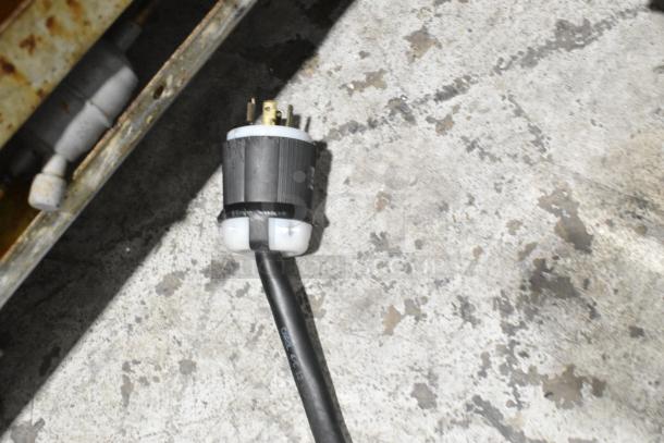 Black electrical cord with a round plug for a Taylor C723-33 ice cream machine on a textured concrete floor.