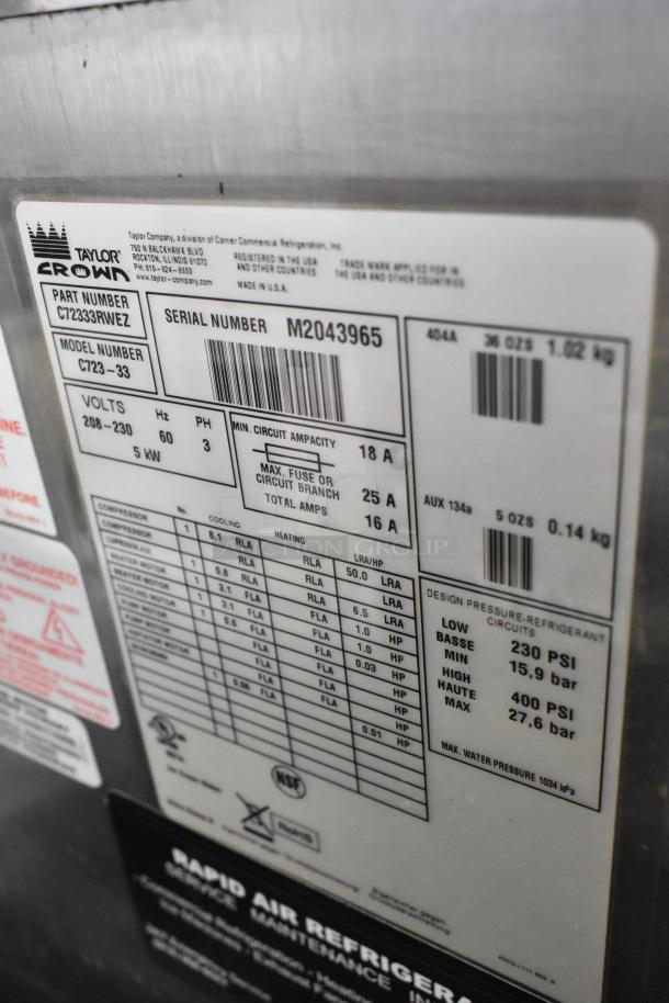 Taylor C723-33 stainless steel commercial soft serve ice cream machine, water-cooled, 2 flavors with twist, on casters, 208-230V, 3 Phase. Labels indicate voltage, serial number M2043965, and refrigerant specs.